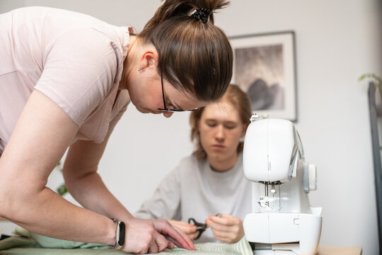Woman preparing fabric while teenager cuts beside sewing machine

