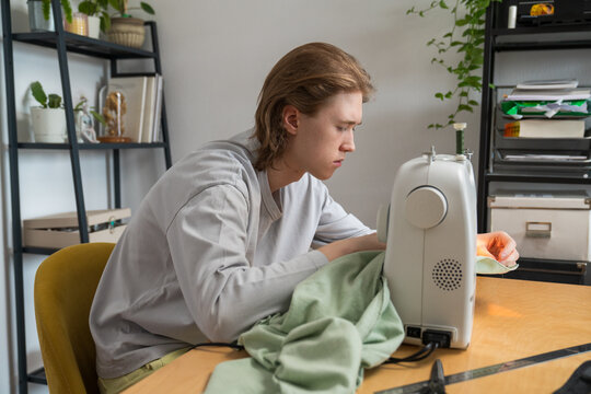 Teenager sewing green fabric with machine at home