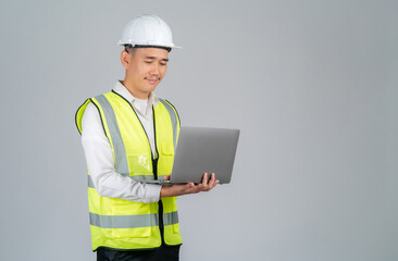 Smiling young Asian engineer or worker working with laptop in studio on grey background.