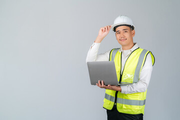 Smiling young Asian engineer or worker working with laptop in studio on grey background.