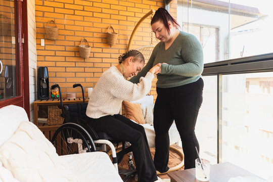 Caregiver Helping Woman in Wheelchair Stand on Terrace