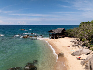 Small seaside hut on a sandy beach surrounded by turquoise water and rocky coastline. Koh Tao, Thailand.