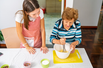 Grandmother whisking ingredients while granddaughter learns secret baking recipes
