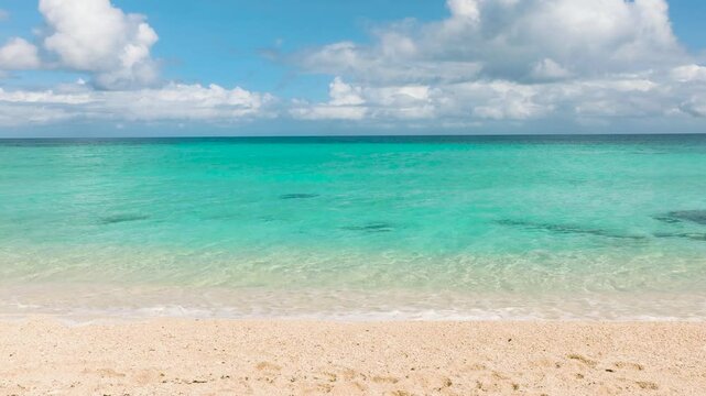 Shimmering turquoise waters stretching to the horizon with soft sand on the shore under fluffy clouds. Boracay Island, Philippines.