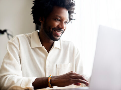 Smiling Man Using laptop In Brightly Lit Modern Setting
