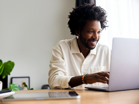 Smiling Man Working on Laptop in Bright and Modern Home Office