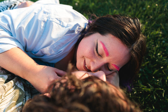 Two non binary people kissing on grass at sunset