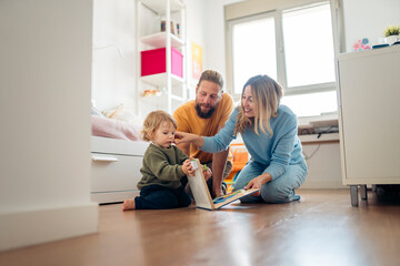 Happy family reading a book and playing with their baby at home