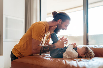 Happy father playing with baby son on sofa at home