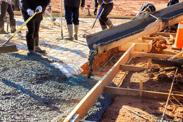 Laborers are actively pouring concrete into wooden frames to foundation slab at construction site...