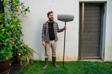 Man gardener posing with garden rake by the lemon plant 