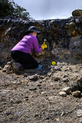 Mature woman rockhounding in Central Oregon, thunderegg pit with tools for digging, recreational hobby hunting for pretty rocks, sledgehammer, gloves, hammer, and pick
