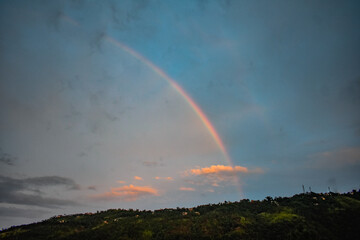 Colorful rainbow arches over lush green hills at sunset in Meghalaya. 