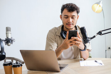Smiling Broadcaster Using Smartphone in Front of Microphone at Home Studio