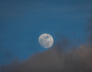 Full moon peeking through atmospheric clouds at twilight.