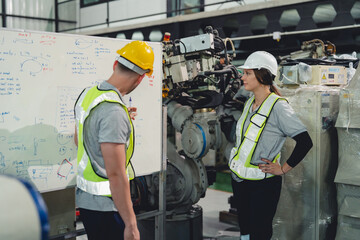 Industrial engineers collaborate in a high-tech factory environment, inspecting robotic machinery...