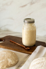 Freshly prepared sourdough bread dough rests on parchment near a container of active starter and a mixing bowl, showcasing the art of home baking.