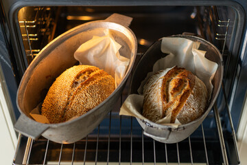 Two golden-brown loaves of bread rest in baking containers inside an oven, their crusts glistening...