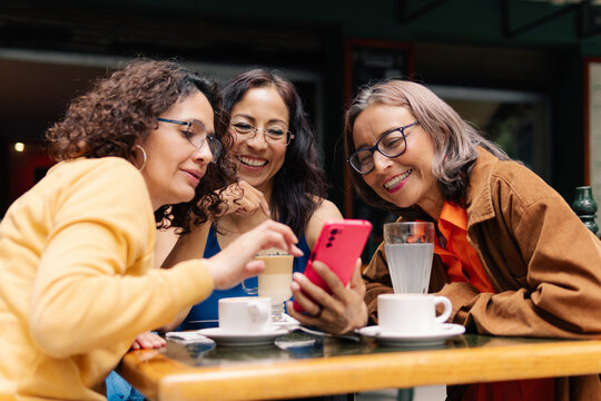 Three Mature Ladies looking At Smartphone In Restaurant.
