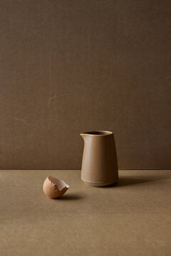 Elegant beige ceramic jug beside an eggshell on earthy background