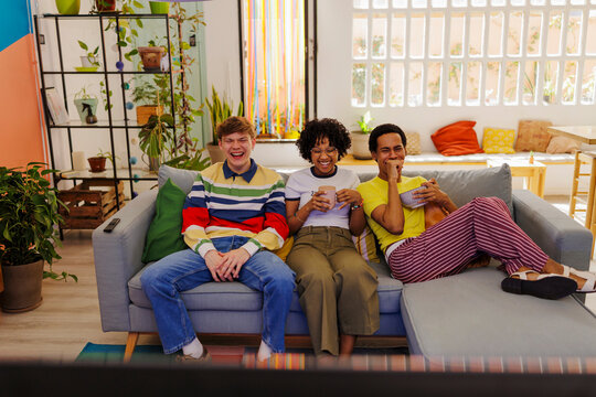 Happy roommates laughing while watching television on colorful room