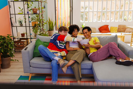 Group of friends relaxing on sofa, watching tv and sharing snacks