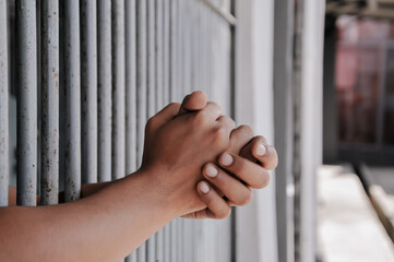 hands of a prisoner behind prison bars on black background	