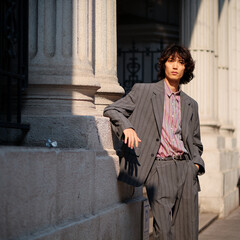 Portrait of handsome Chinese young man wearing gray suit posing in the street, young guy with black curly hair with urban background. Male fashion, cool Asian young man lifestyle.