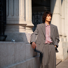 Portrait of handsome Chinese young man wearing gray suit posing in the street, young guy with black curly hair with urban background. Male fashion, cool Asian young man lifestyle.