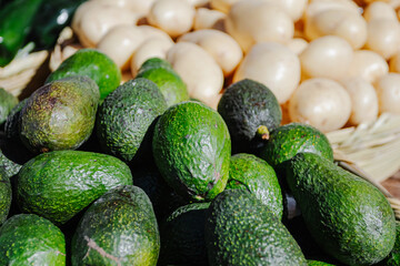 Close-up of fresh green avocados piled in a woven basket at a local outdoor market. The natural lighting highlights their texture and ripeness, ideal for culinary, agricultural, or nutritional