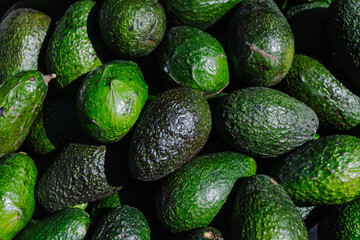 Close-up of fresh green avocados piled in a woven basket at a local outdoor market. The natural lighting highlights their texture and ripeness, ideal for culinary, agricultural, or nutritional
