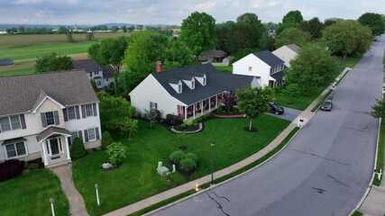 Luxury Two-story Houses with american flag and well-kept front yard. Aerial approaching shot. Single family houses in quiet and noble suburb. Agricultural farm fields in distance. Pennsylvania, USA. - Powered by Adobe
