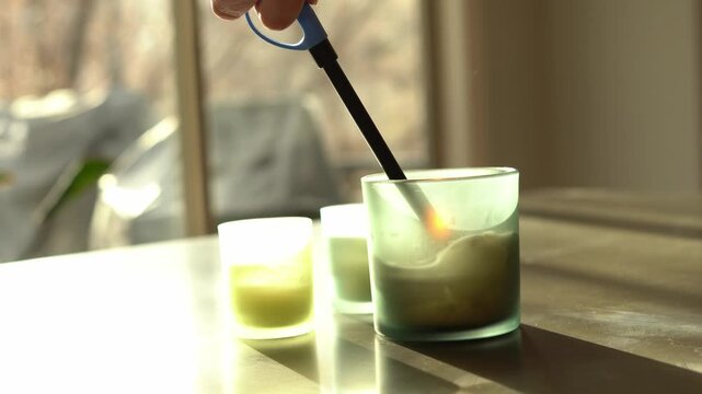 Hand lighting a candle in green frosted glass container with long lighter low shallow depth of field