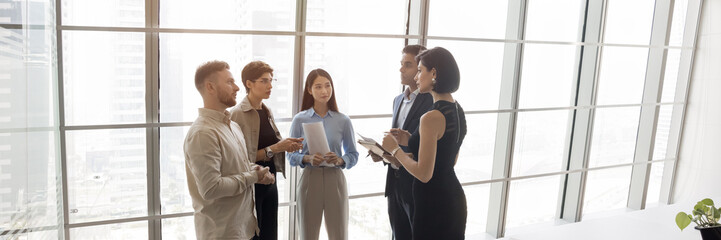Group of five processionals discussing work-related matters gathered in modern office standing...