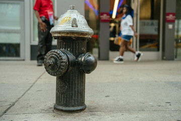 People pass by a weathered fire hydrant on the sidewalk. The scene captures New York's busy street rhythm.