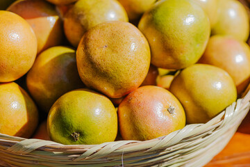 Close-up of ripe grapefruits in a woven basket, displayed at an outdoor market. Their shiny skin and vibrant color make them perfect for use in content related to nutrition, citrus fruits, and healthy