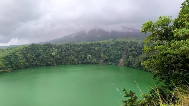 Aerial view of  Lake Tolire in Ternate, Indonesia, with vibrant green water surrounded by lush forest.