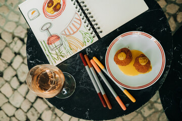 Close-up of sketchbook, snacks, and wine on cafe table