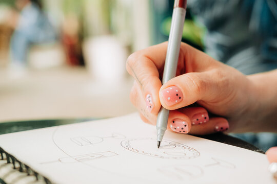 Close-up of female hand sketching in notebook with fine liner pen