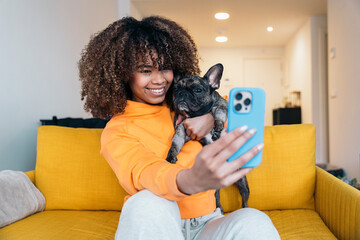 Young woman taking selfie with french bulldog on sofa at home