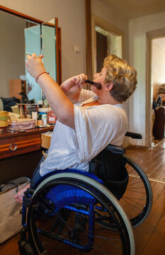 A woman with a disability does her makeup in front of the mirror.
