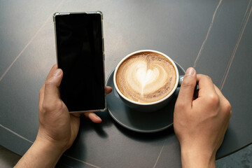 Close-up of a man's hands drinking coffee and looking at his phone in the courtyard