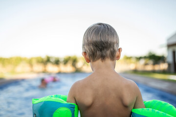Little boy standing by the pool with floaties, about to jump in