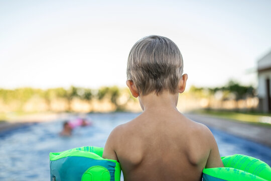 Little boy standing by the pool with floaties, about to jump in