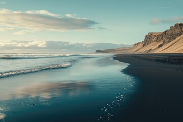 Picturesque black sand beach meets the ocean. Calm waves gently caress the shore. Dramatic cliffs rise in the background