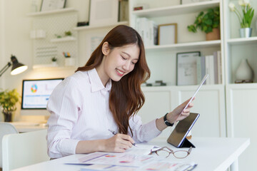 Smiling businesswoman reviewing financial reports at desk, with charts and graphs in a modern office.