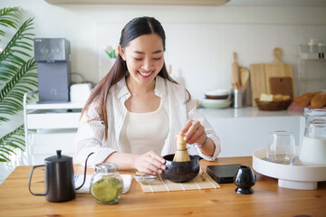 Smiling asian woman preparing matcha using a bamboo whisk and authentic Japanese tools.