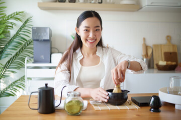 Smiling asian woman preparing matcha using a bamboo whisk and authentic Japanese tools.