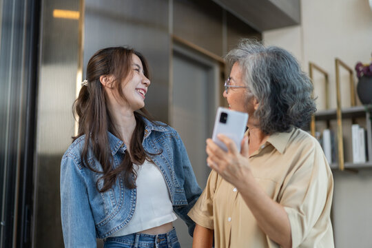Asian senior mother and daughter smiling and talking using smartphone browsing social media, shopping online, watching movies or series, enjoying entertainment digital connection and bonding at home
