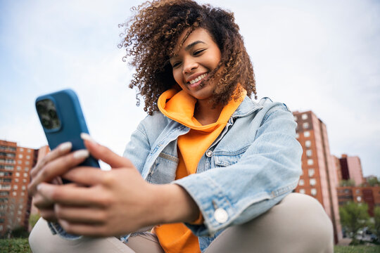 Smiling young woman using smartphone outdoors in urban park